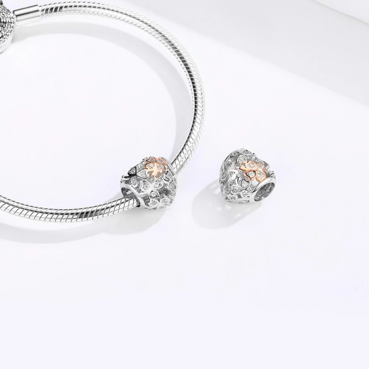 Ażurowy charms Serce Koniczynki prezentowany na bransoletce modułowej. Zawieszka Amélioré ozdobiona białymi cyrkoniami i czterolistną koniczynką w kolorze rose gold, łącząca symbolikę miłości i szczęścia. Pasuje do produktów Pandora i Apart.