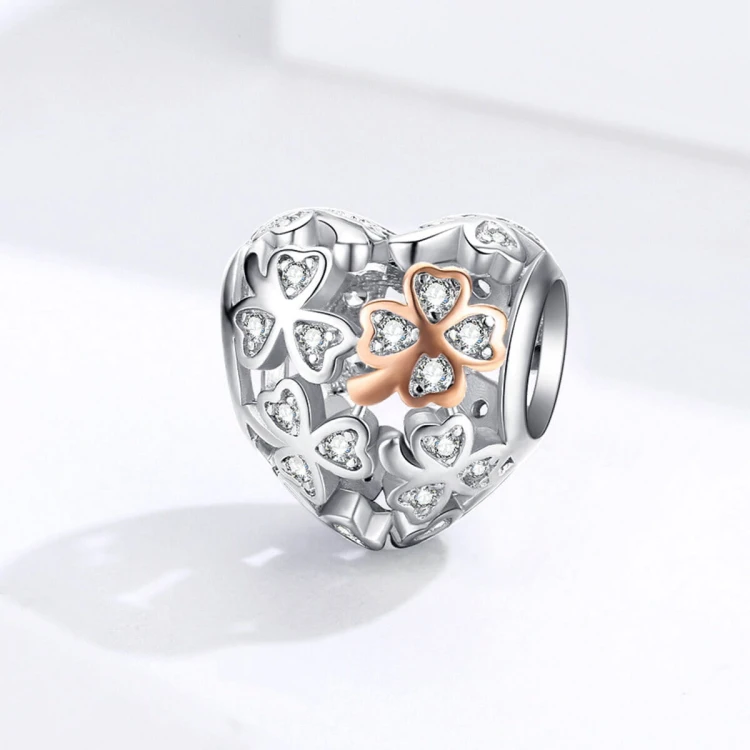 Ażurowy charms Serce Koniczynki ozdobiony białymi cyrkoniami oraz czterolistną koniczynką w kolorze rose gold. Symboliczna zawieszka Amélioré łącząca motyw miłości, szczęścia i pomyślności, kompatybilna z bransoletkami Pandora i Apart.